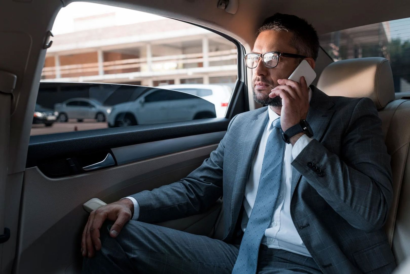 Geschäftsmann im Anzug telefoniert auf der Rückbank eines komfortablen Taxis während der Fahrt.